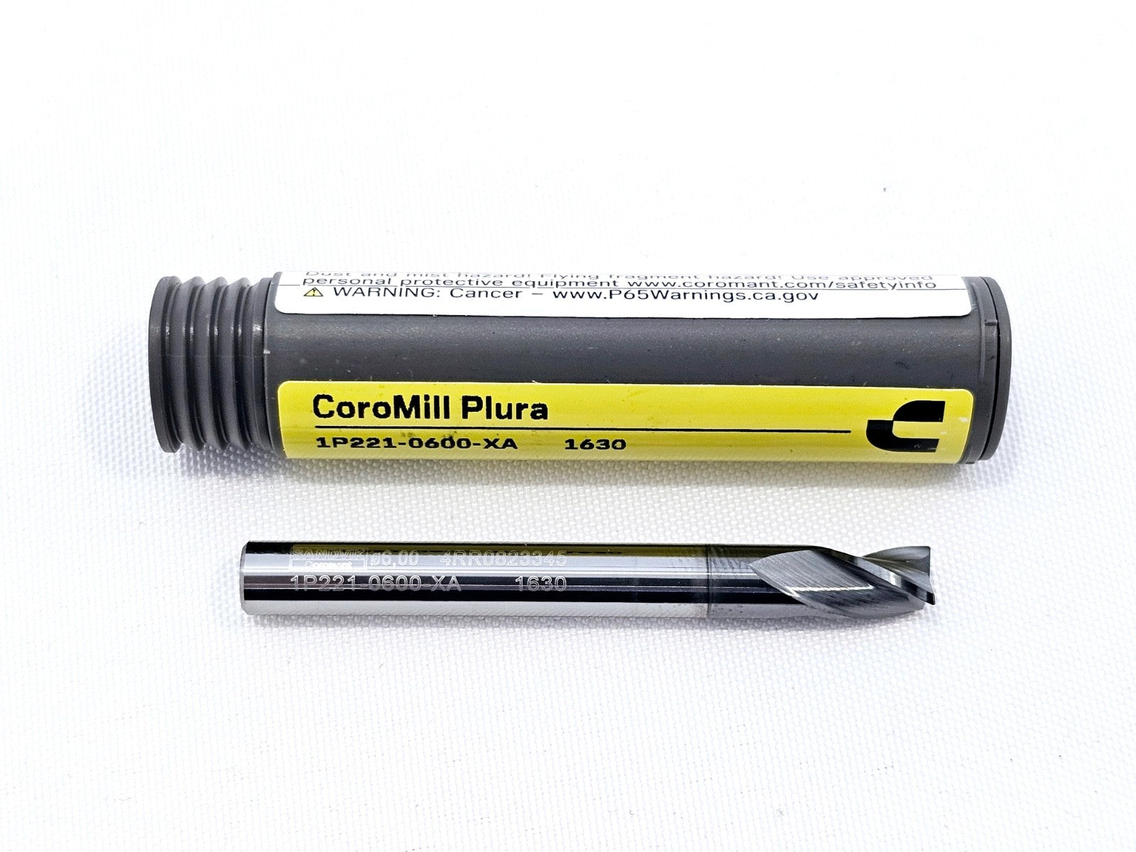 Sandvik Coromant CoroMill Plura 1P221-0600-XA 1630 6mm end mill beside open grey storage tube, showing AlCrN-coated flutes