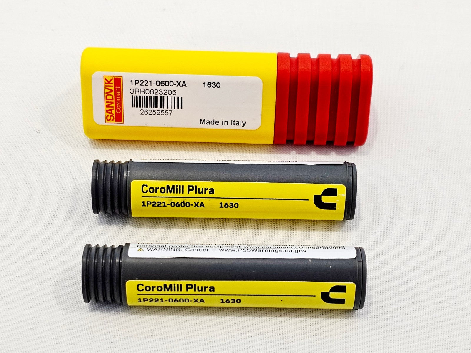 Three Sandvik Coromant CoroMill Plura 1P221-0600-XA 1630 end mills — one in yellow/red case and two in grey storage tubes