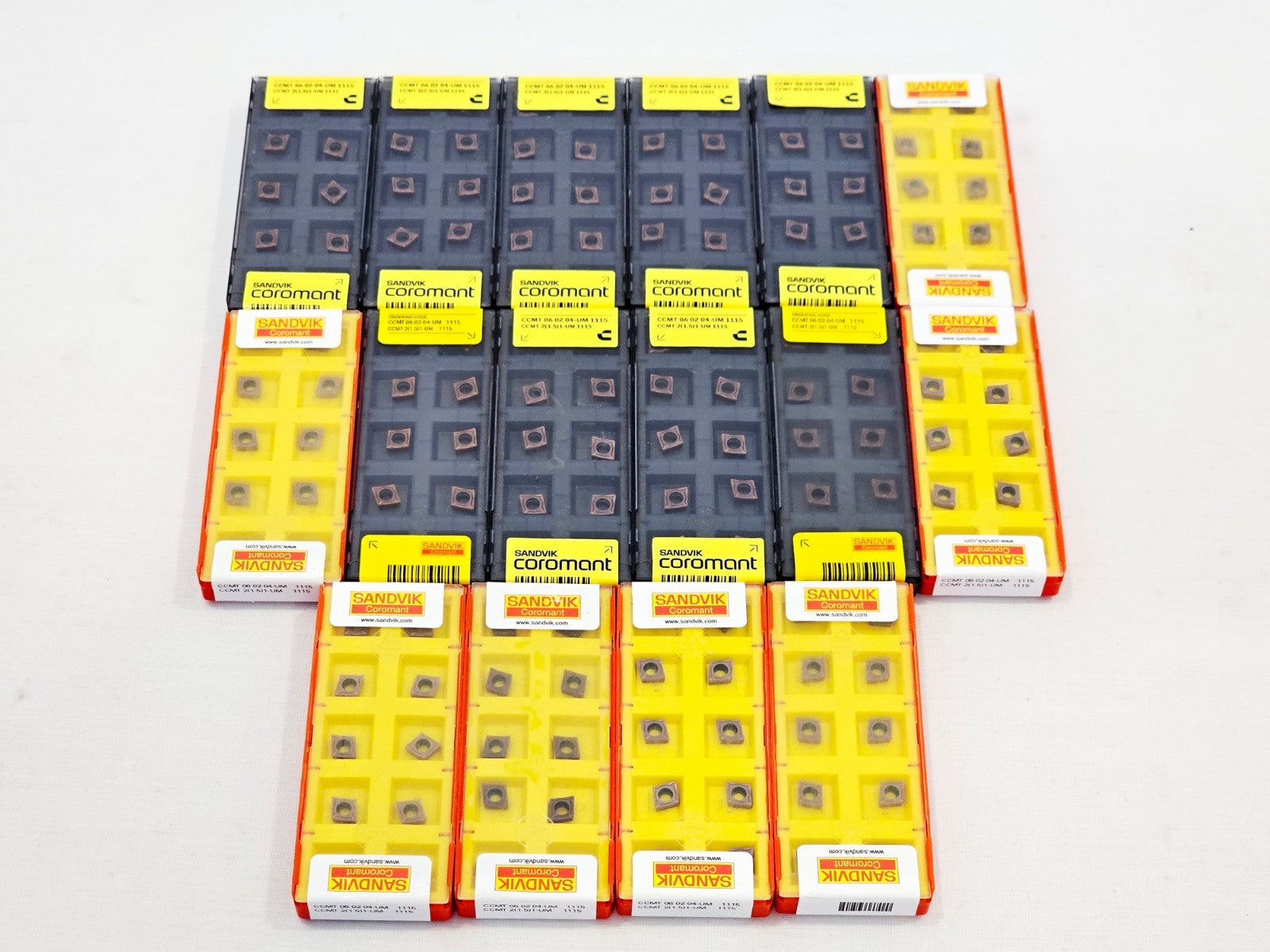 16x Sandvik Coromant CCMT 060204-UM 1115 carbide insert packs — mixed dark and yellow trays overhead view
