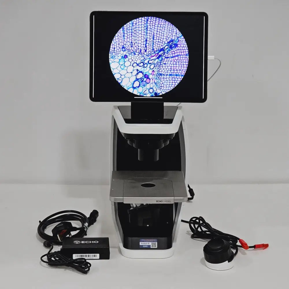 ECHO Rebel REB-01-D microscope front view with iPad display showing stained tissue sample, power adapter, focus wheel, and accessories laid out