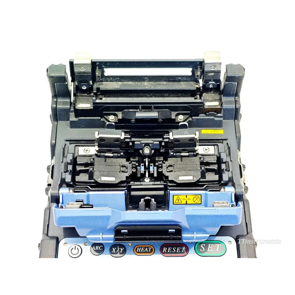Fujikura FSM-62S+ splicer top-down view with wind protector open, showing V-grooves, fibre clamps and HOT warning label